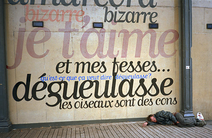 A man sleeping in front of a movie theater next to the bassin de la Villette in Paris.